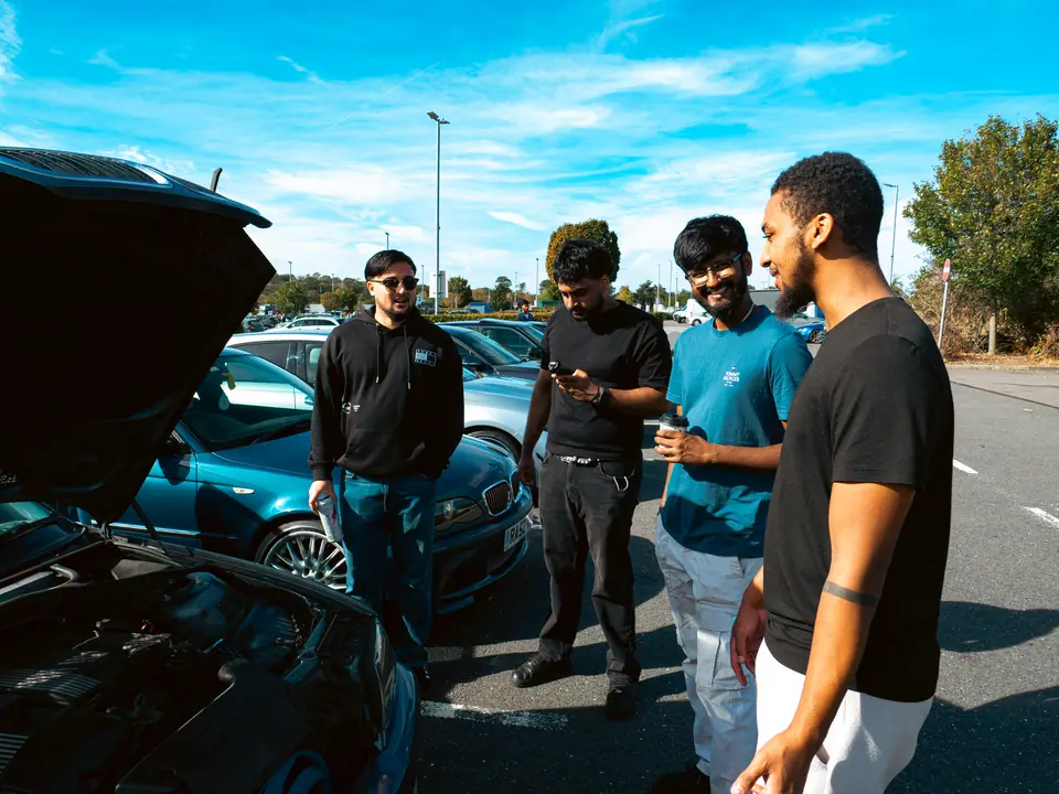 Four friends talking beside an open bonnet, a blue BMW 3 Series behind them
