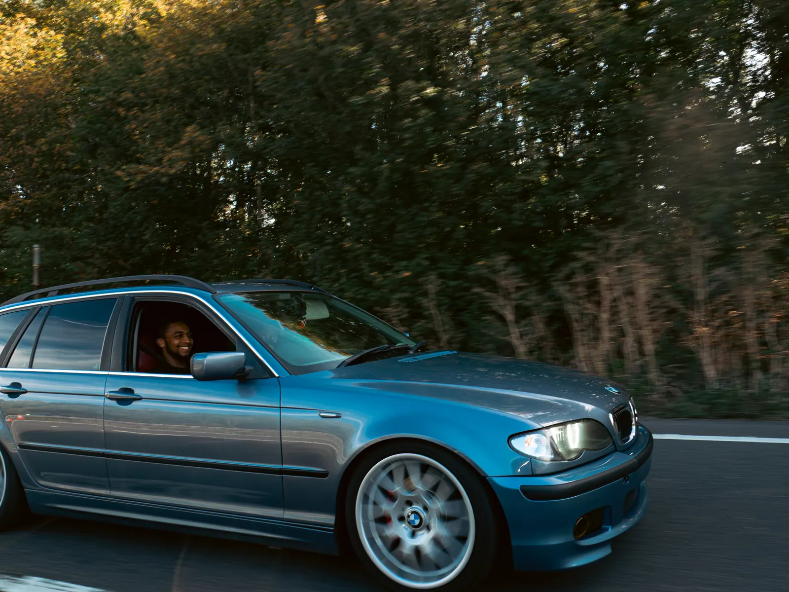 Blue BMW 3 Series Touring on deep-dish wheels, driver waving