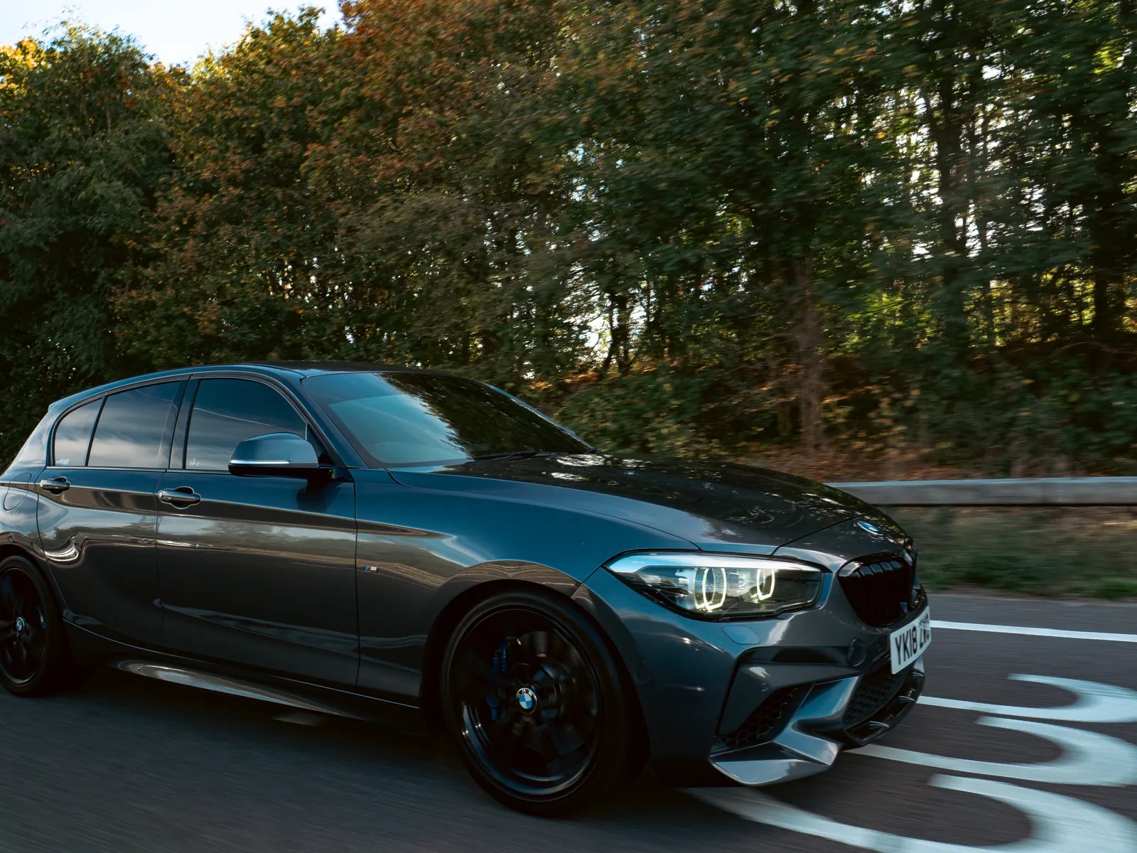Grey BMW 1 Series on black wheels, tracking alongside