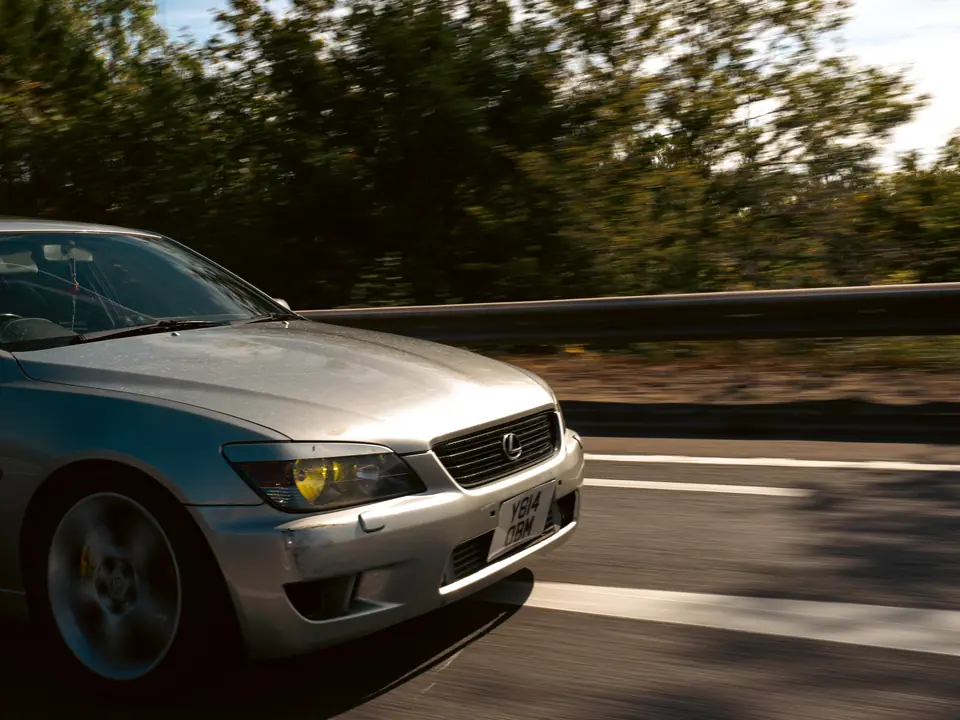 Silver Lexus IS with yellow fog lights, close rolling shot