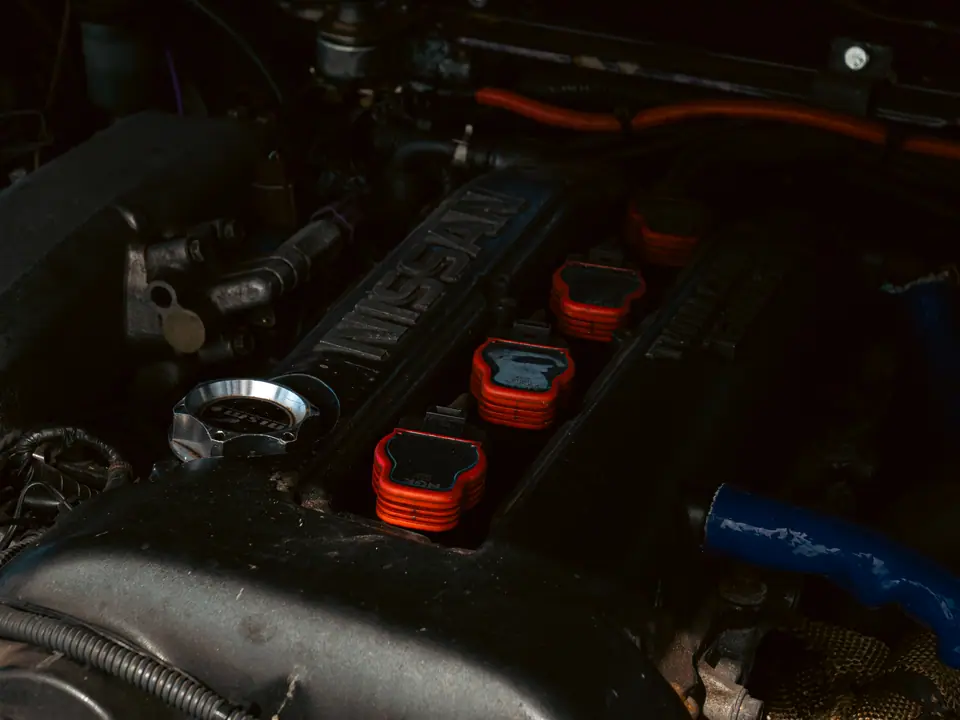 Nissan cam cover with red coil packs and a blue silicone hose