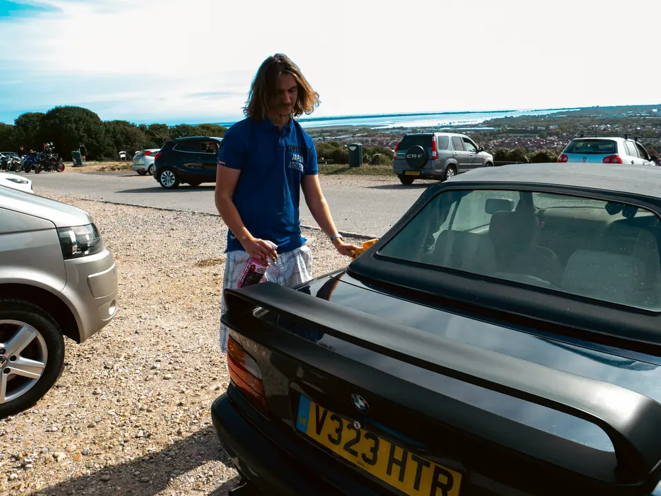 Leaning on the boot of the dark blue BMW convertible