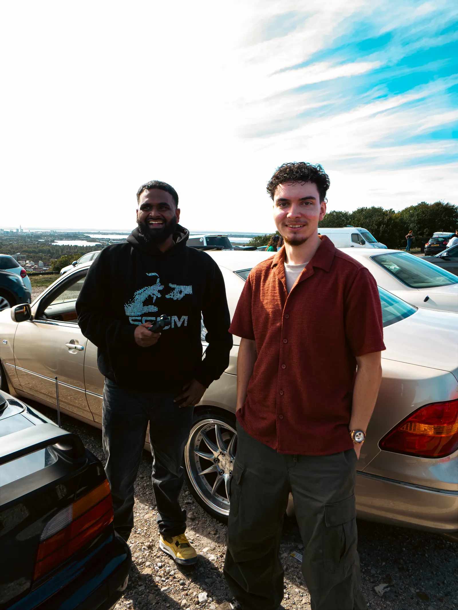 Two friends smiling in front of a gold Lexus LS