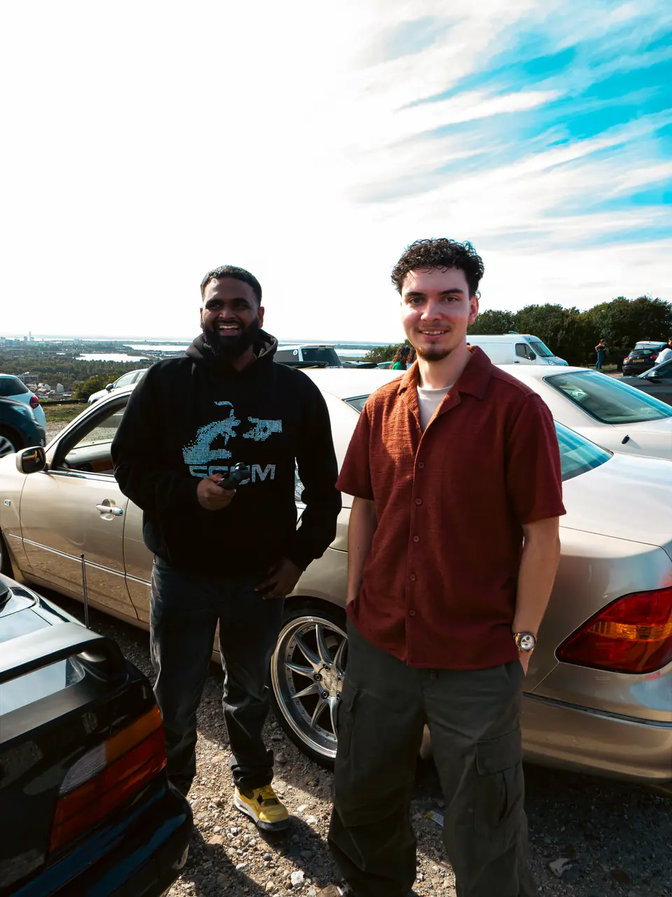 Two friends smiling in front of a gold Lexus LS