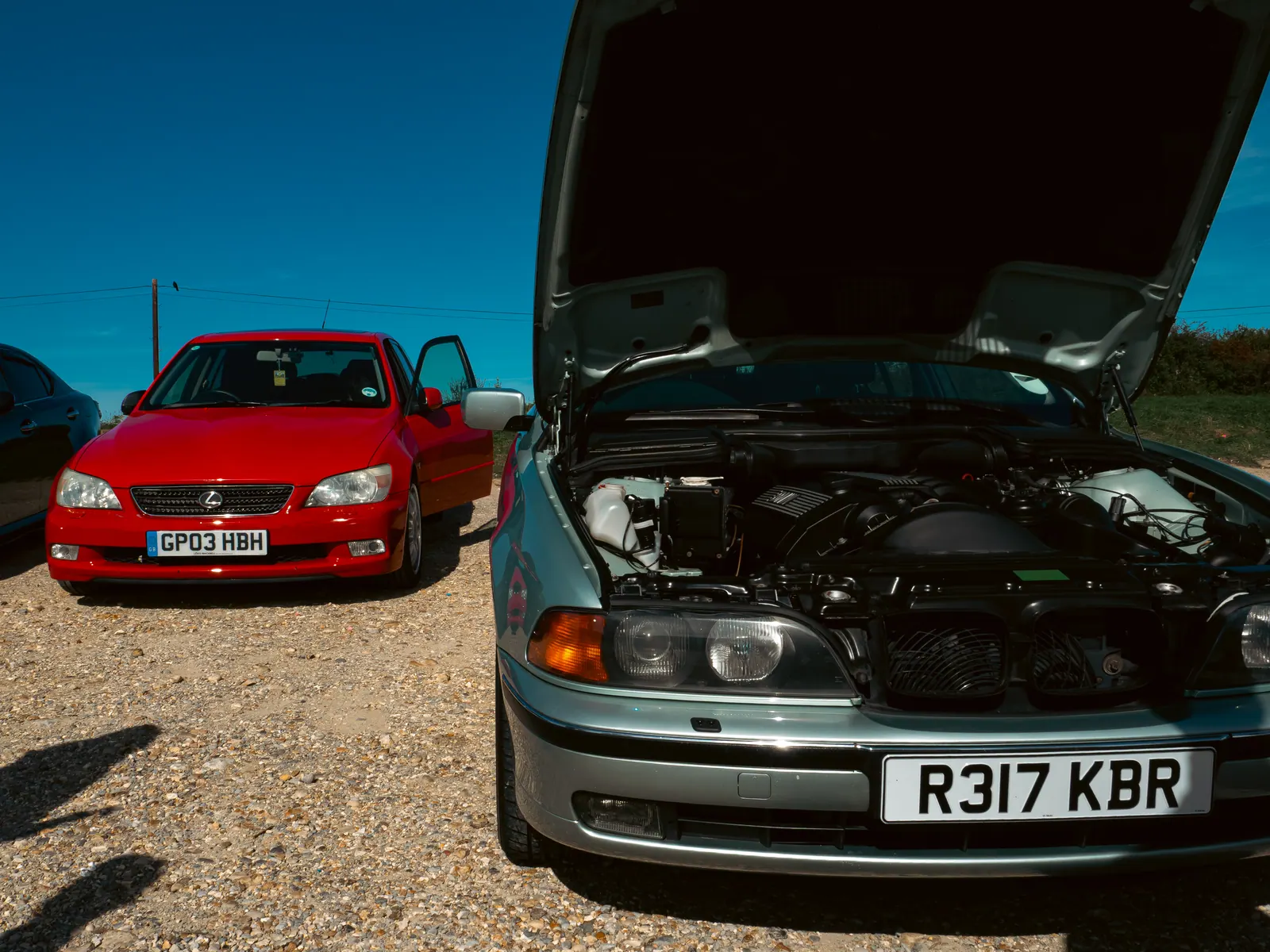 Red Lexus IS beside a silver BMW 5 Series with its bonnet up