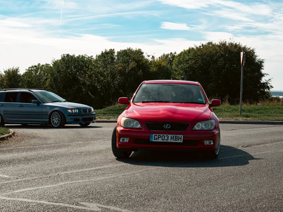Red Lexus IS heading out, blue BMW 3 Series Touring behind