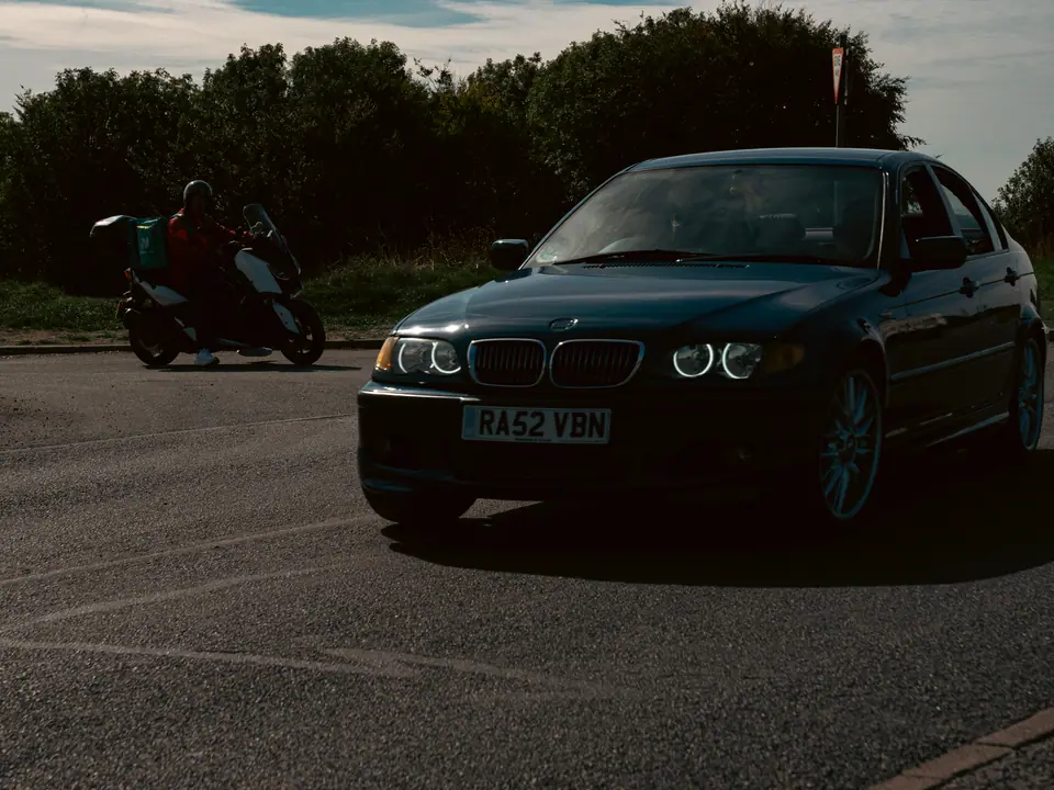 Blue BMW 3 Series saloon close up, a scooter passing