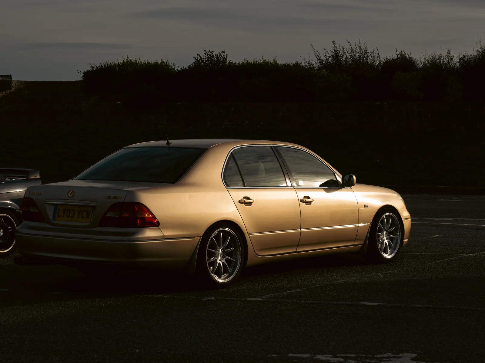 Gold Lexus LS, three-quarter rear, at dusk