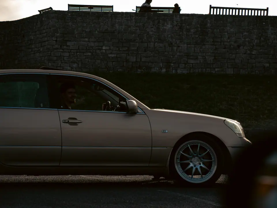 Side profile of the gold Lexus LS under the old wall